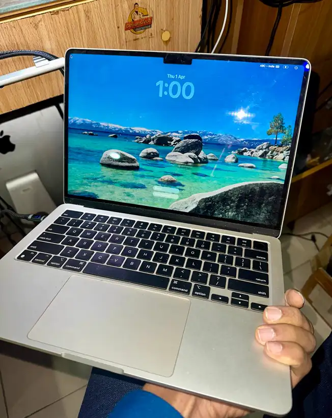 A repaired MacBook Air powered on and running, held up in the DelsonsTech workshop.