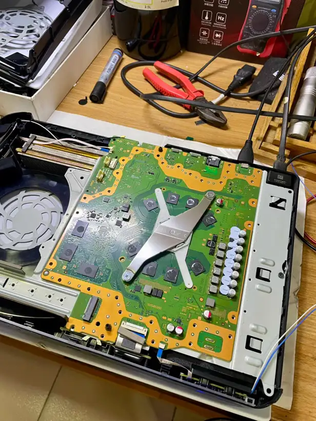 An original PlayStation 5 opened on the bench with the motherboard, cooling fan and heatsink bracket exposed.