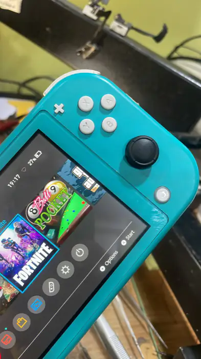 The same Nintendo Switch Lite with a new analogue stick fitted and the console powered on at the home menu.